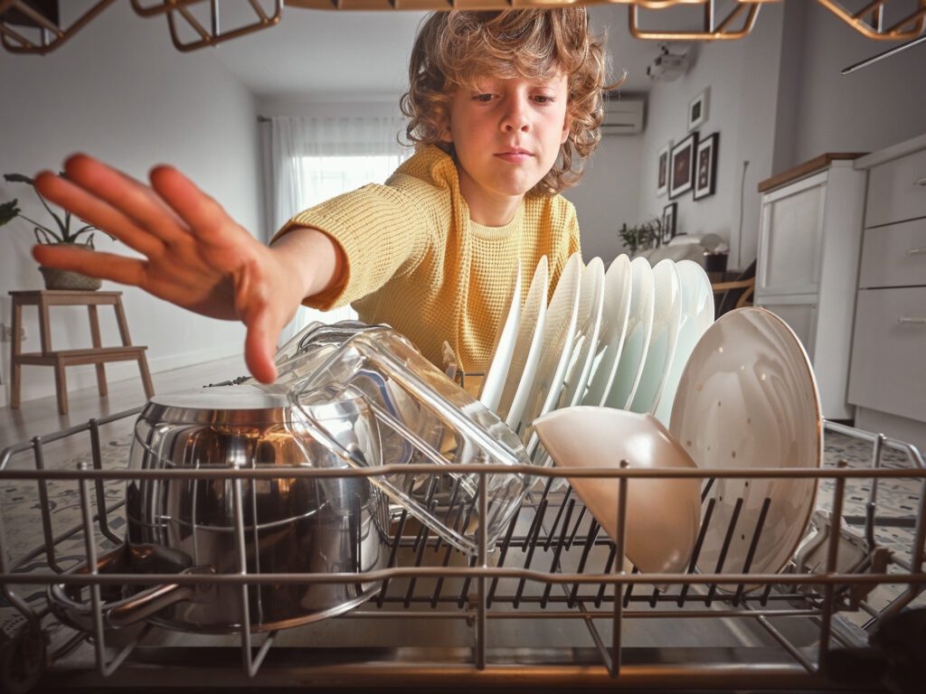cute boy casual wear unloading modern dishwasher with various clean dishware household routine light kitchen home